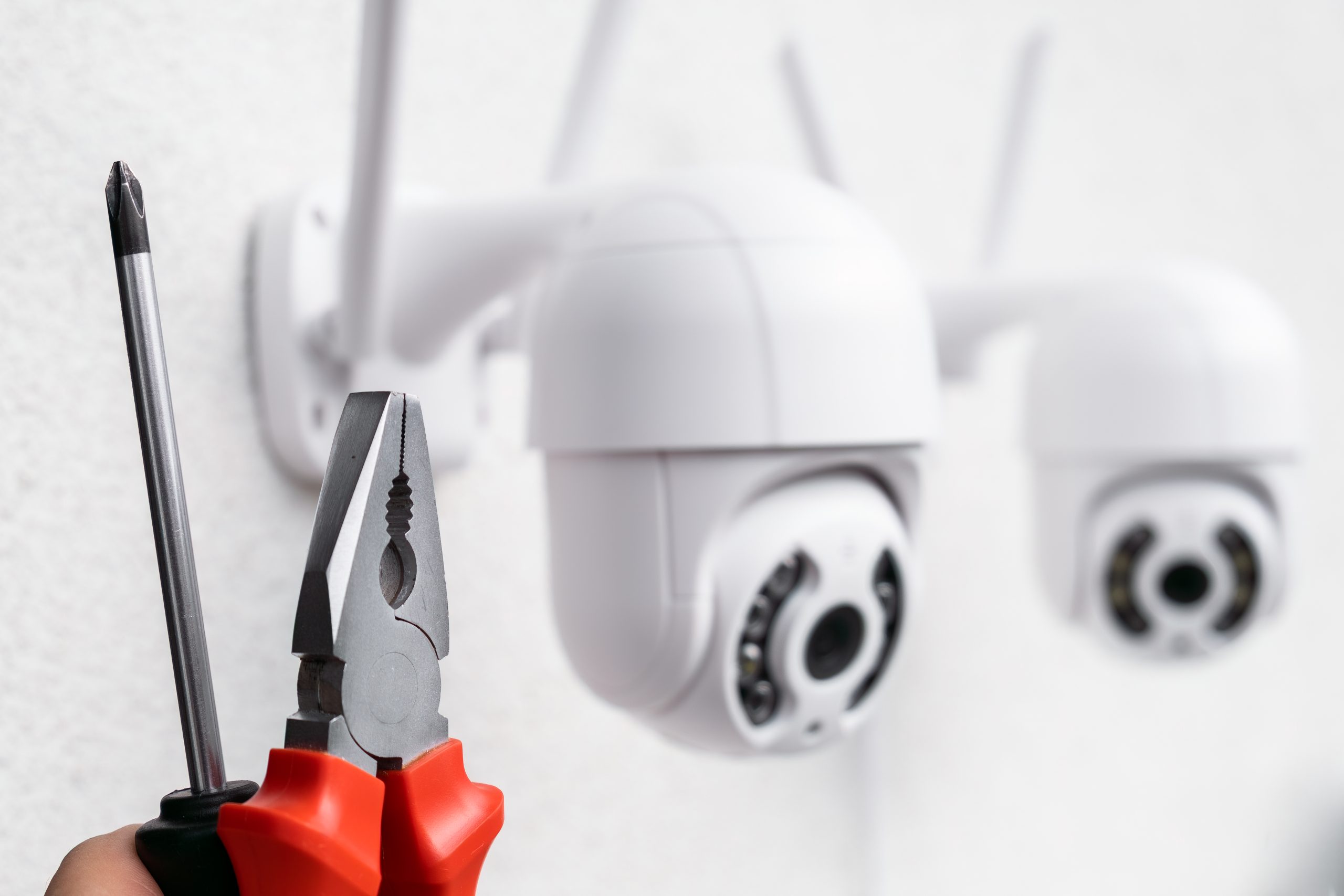 Technician installing CCTV camera using pliers and screwdriver on wall mount